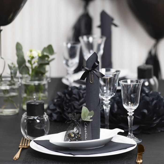 Decoraciones para mesa en negro con flores de papel, globos, una servilleta enrollada como una torre y tarjetas de lugar.