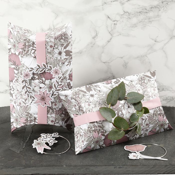 Cajas almohadas decoradas con cinta rosa, un aro de metal y recortables de flor.