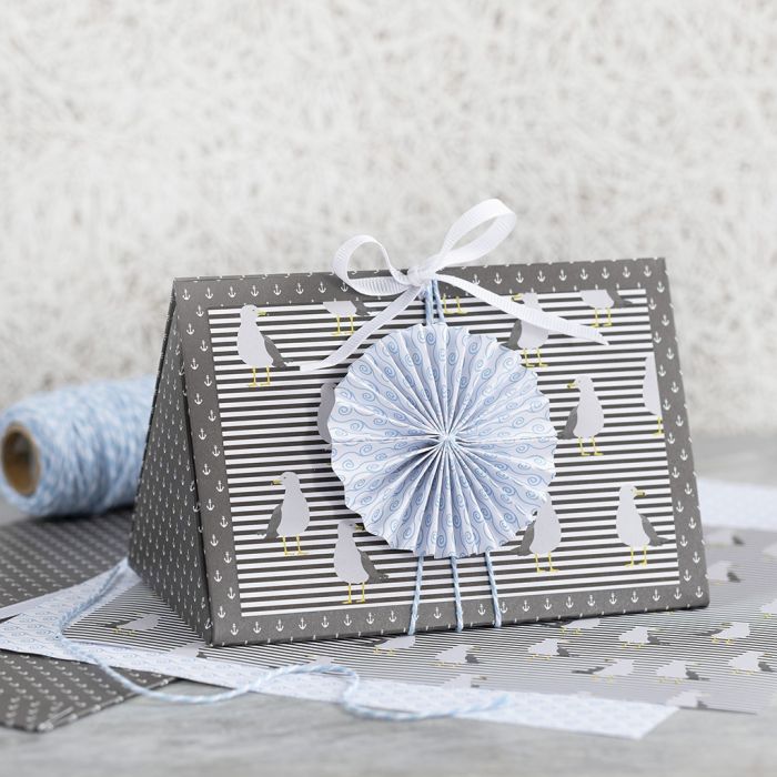 Una caja de regalo azul oscura decorada con una roseta azul y papel de diseño.