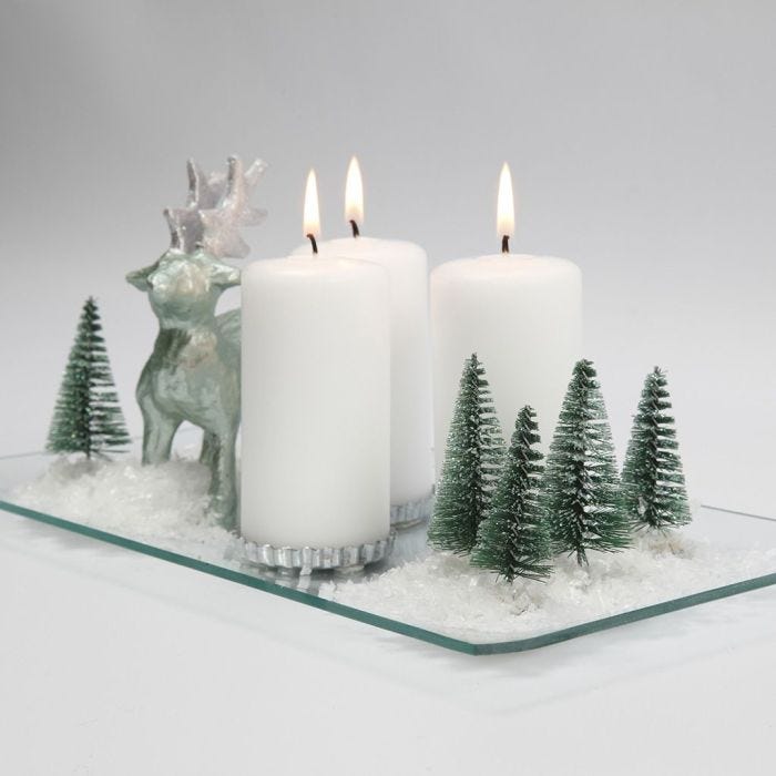 Una decoración de Navidad con velas, renos, árboles y nieve en un plato de vidrio