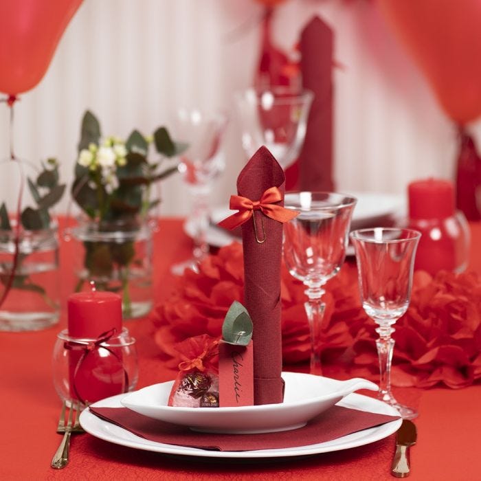 Decoraciones para mesa en rojo con flores de papel, globos, una servilleta doblada como una torre y tarjetas de lugar.