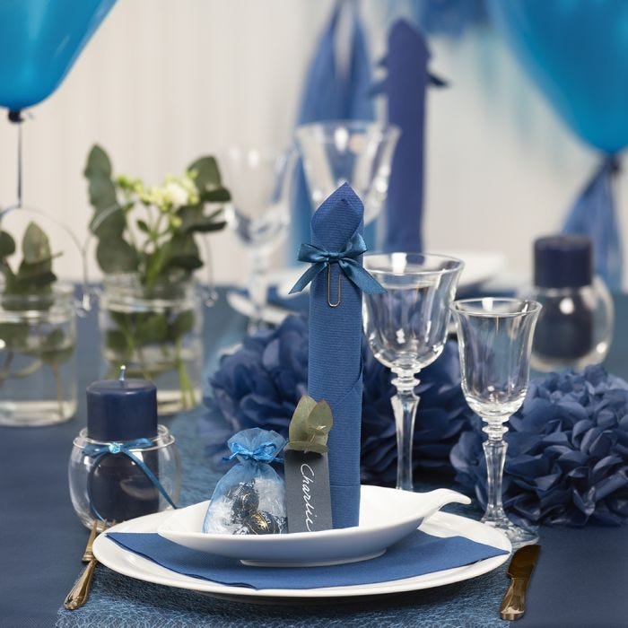 Decoraciones para mesa en azul oscuro con flores de papel, globos, una servilleta doblada como una torre y tarjetas de lugar.