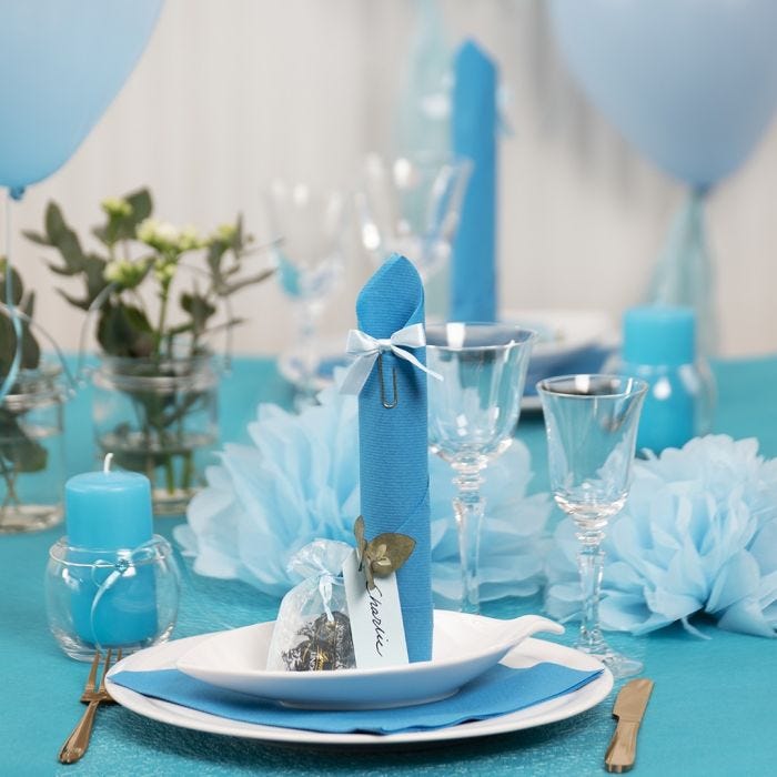 Decoraciones para la mesa en azul claro con flores de papel, globos, servilleta doblada como una torre y tarjetas de lugar.