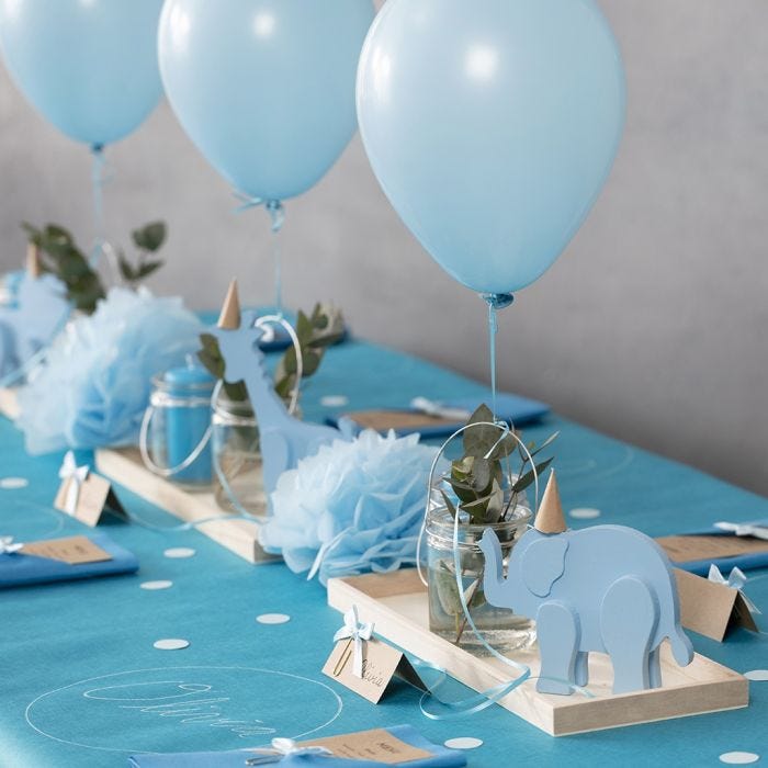 Decoraciones para bautizo con animales de madera, servilletas dobladas, minutas, pompones y globos de helio.