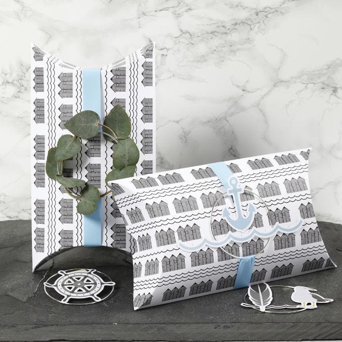 Cajas almohadas decoradas con cinta azul, un aro de metal y decoraciones de recortables marítimos.