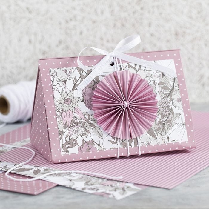 Una caja de regalo rosa con una roseta y papel de diseño.