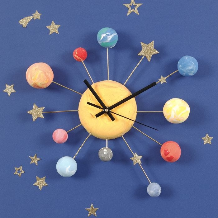 Un reloj de pared decorado con planetas de Silk Clay, pegatinas de estrellas y alambre para bonsai.