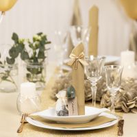 Decoraciones de mesa en dorado con flores de papel, globos, una servilleta doblada como una torre y tarjetas de lugar.